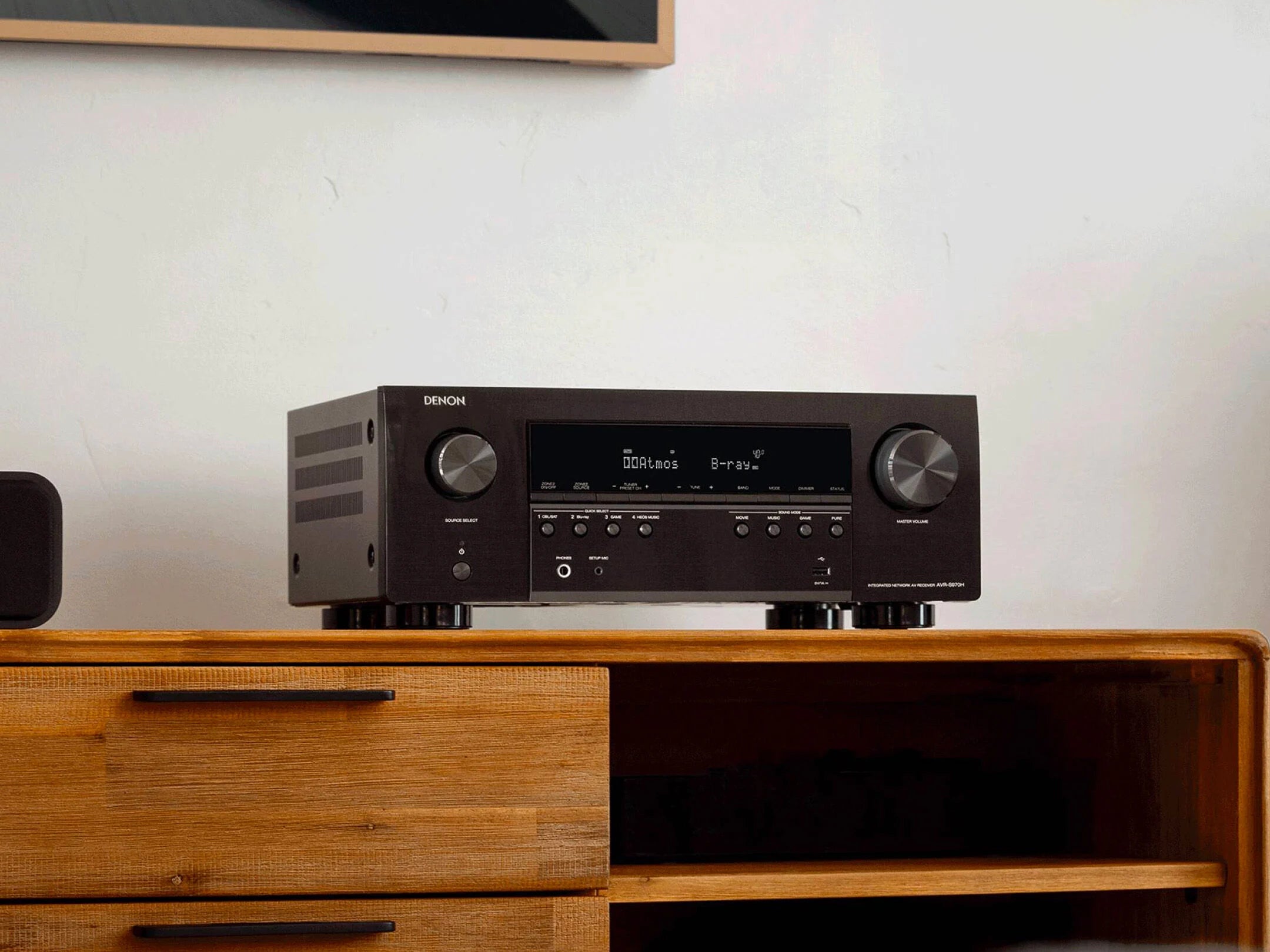 Denon AV receiver on a wooden cabinet with a white wall background