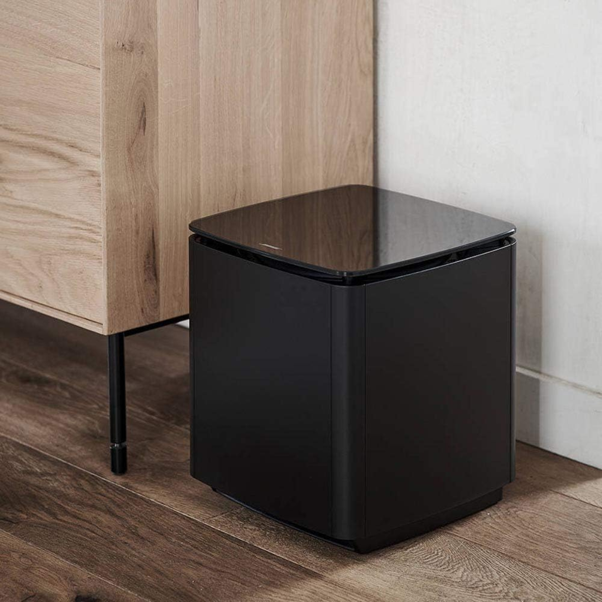Black subwoofer on a wooden floor against a wooden wall.