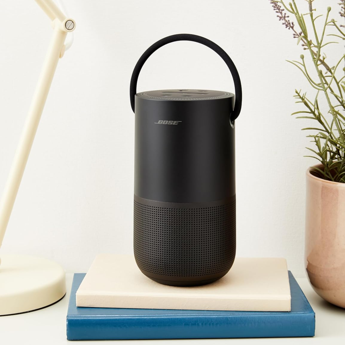 Black Bose speaker on a stack of books with a plant and lamp in the background