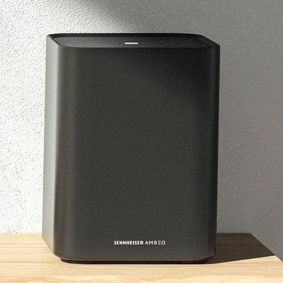 Black Sennheiser AMBEO speaker on a wooden surface with a gray wall background