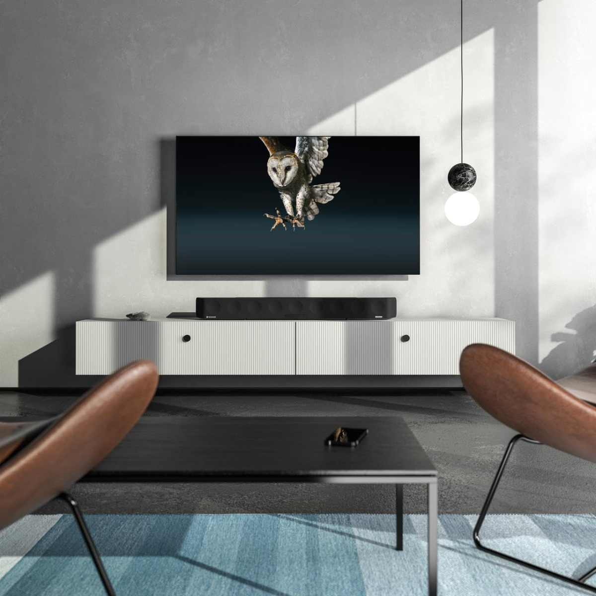 Modern living room with a TV displaying an owl, surrounded by minimal furniture and sennheiser soundbar.