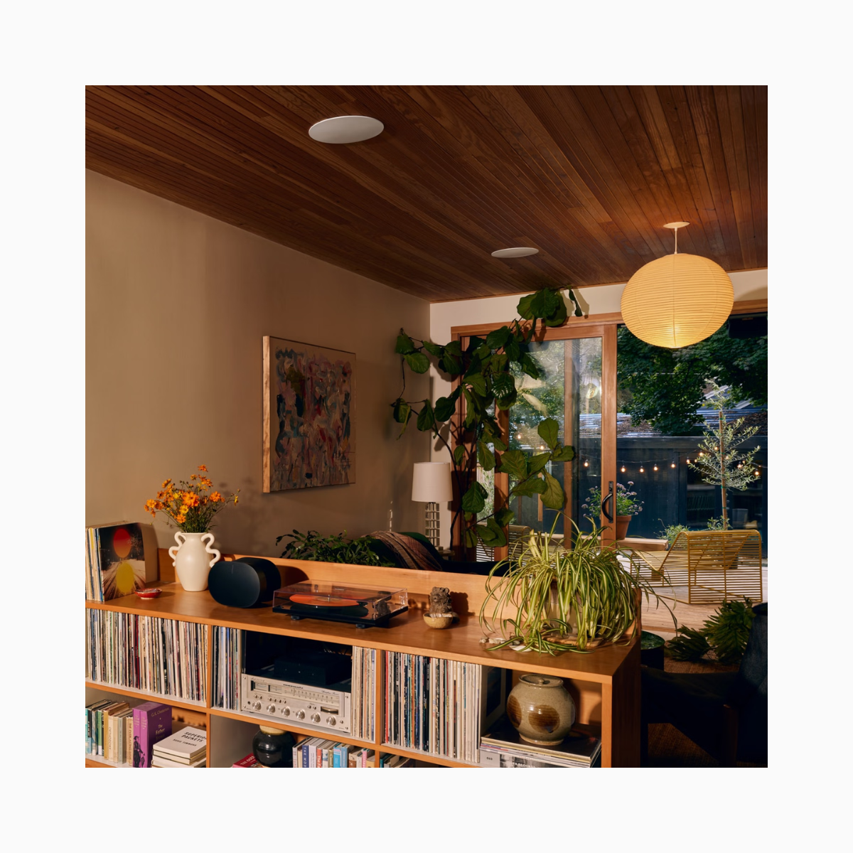 Living room with wooden bookshelf, plants, and a large window.