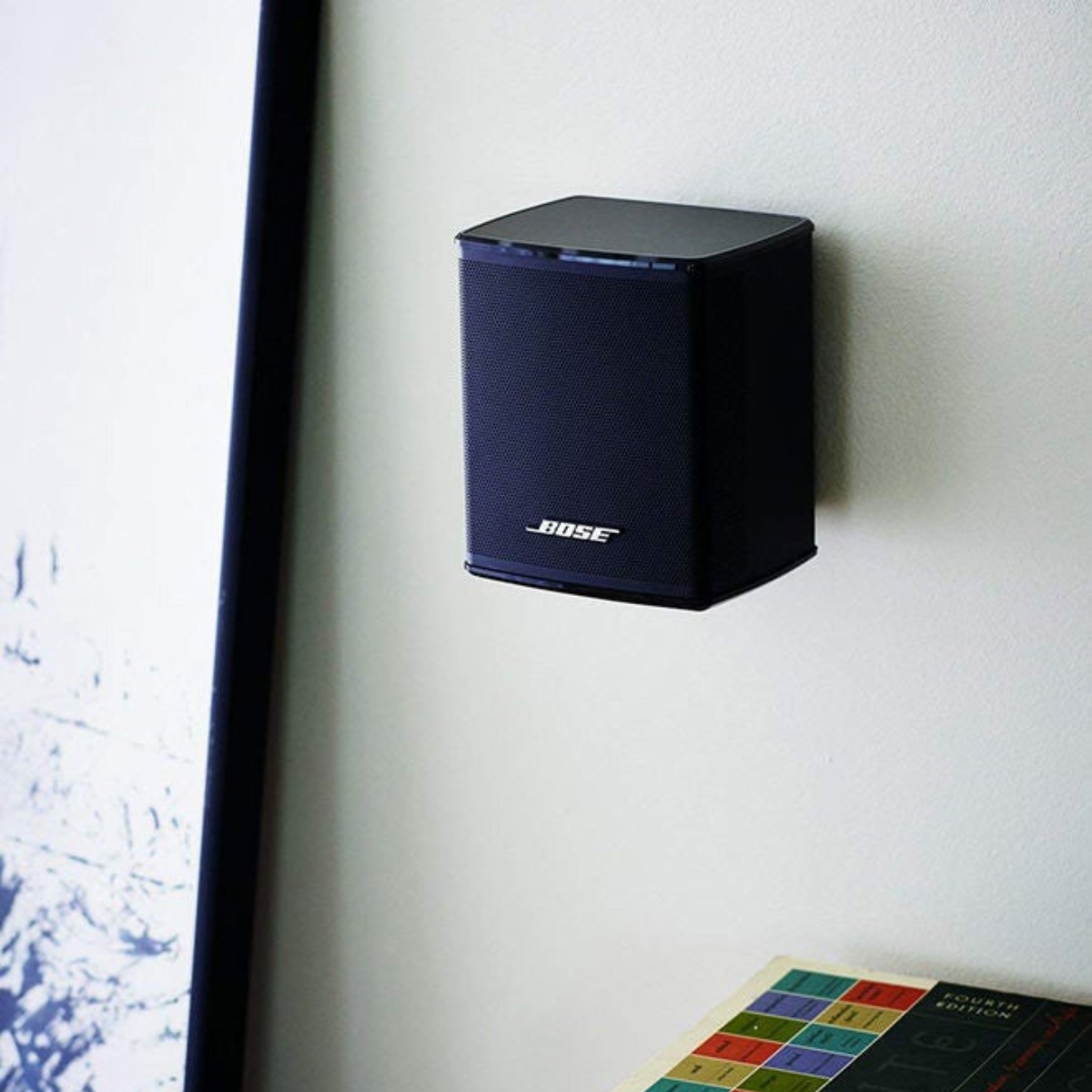 Black Bose speaker mounted on a white wall next to a television.