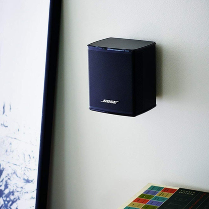 Black Bose speaker mounted on a white wall next to a television.
