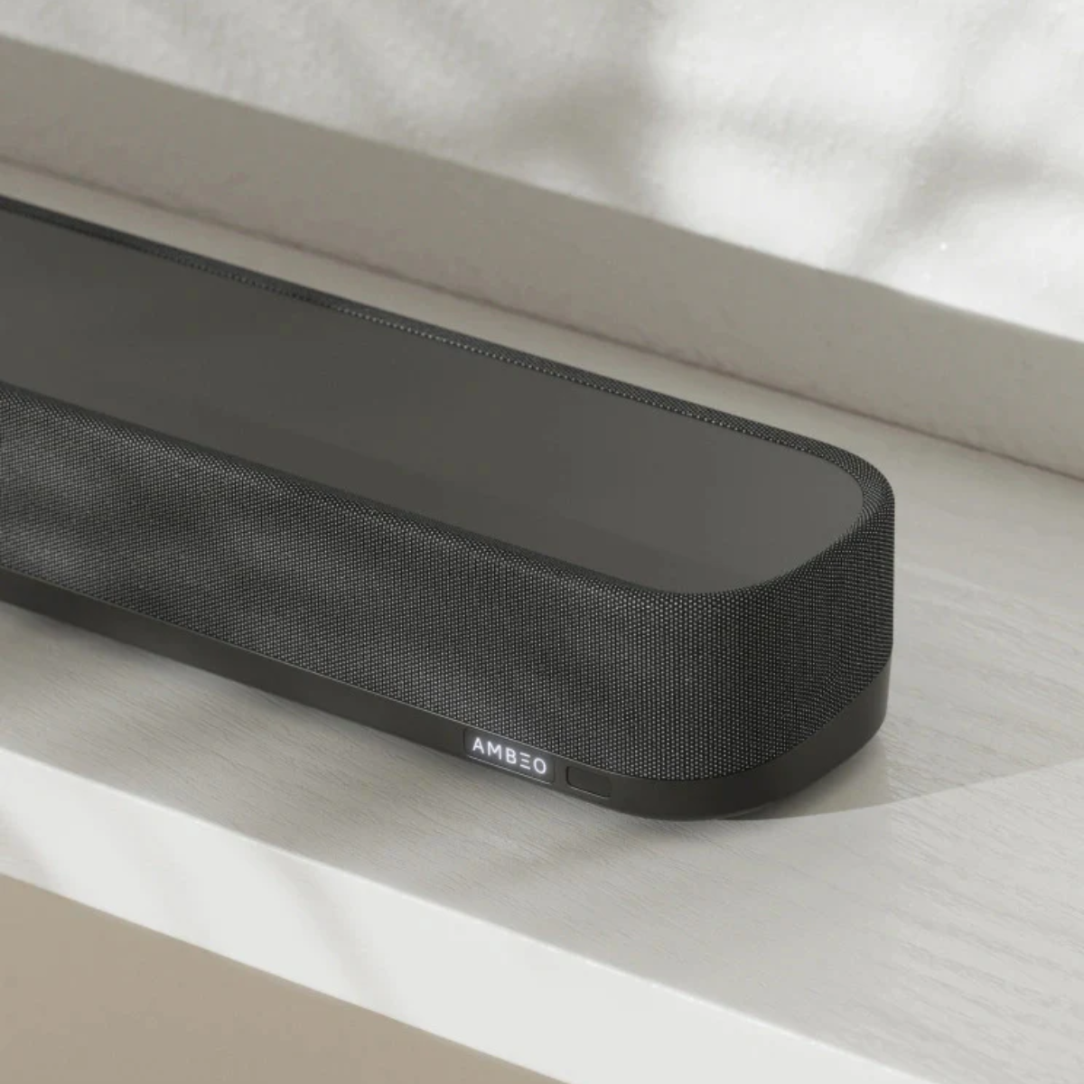Black soundbar with 'AMBEO' branding on a light wooden surface