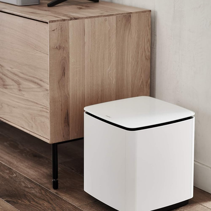 Bose Bass Module 700 wireless subwoofer in white placed beside a wooden cabinet
